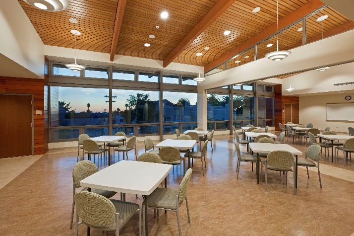 Inside view of a large classroom set up with square card tables and four cushioned chairs around each table.